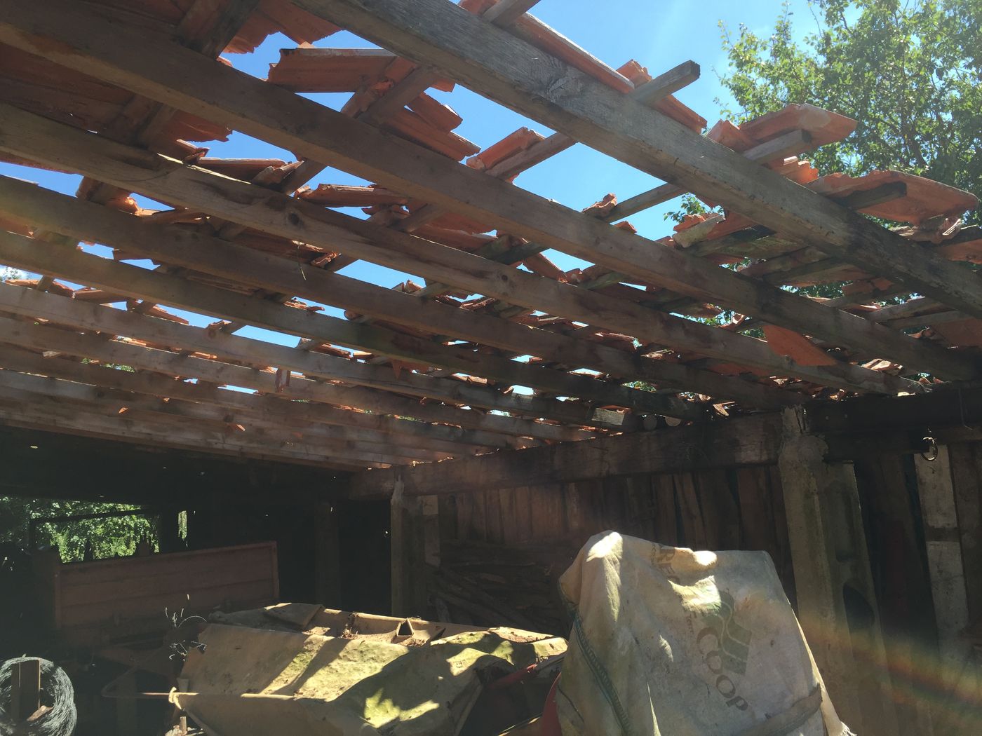 Charpente de hangar vue de dessous, tuiles brisées sur les liteaux